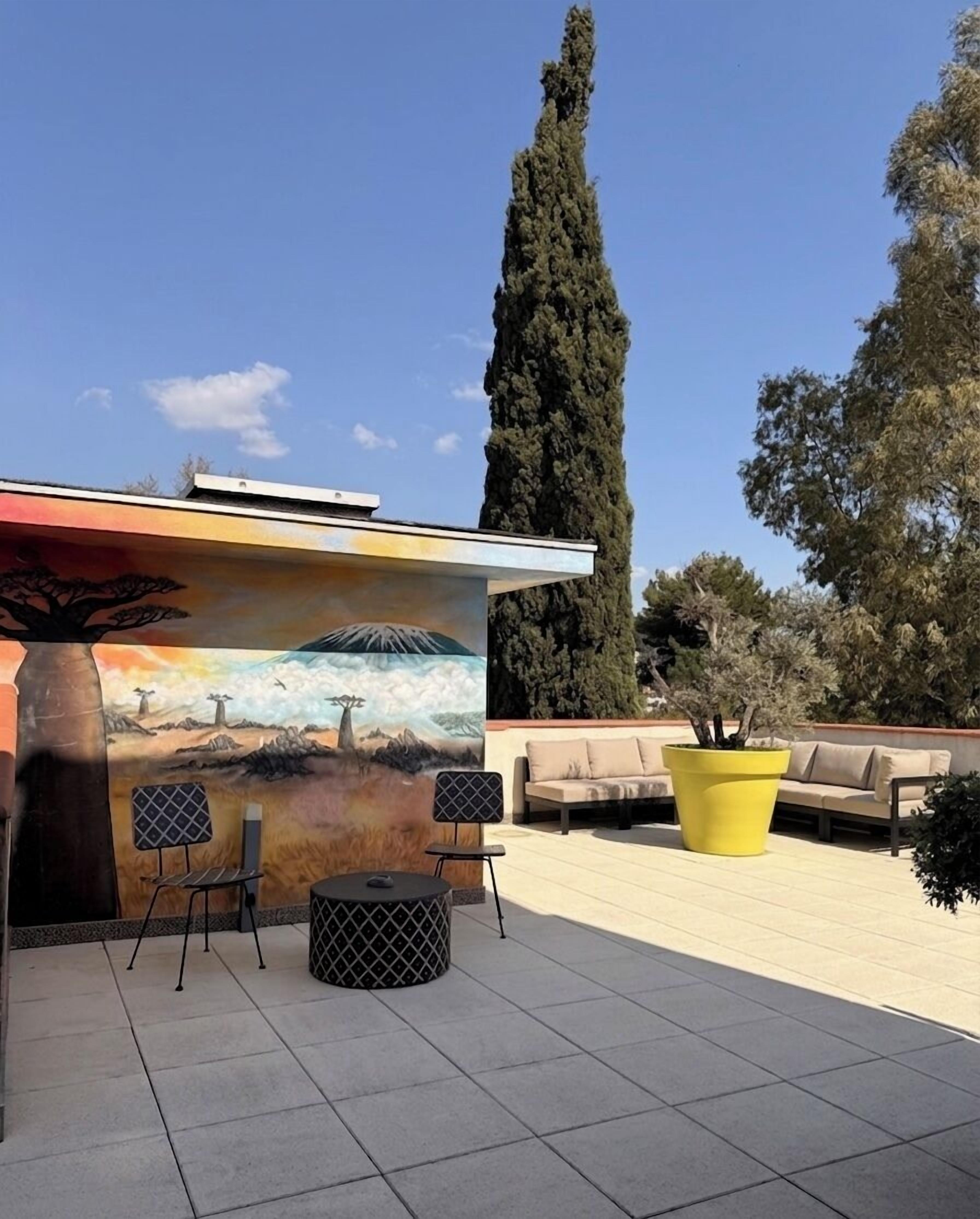 A patio area with a mural, outdoor seating, and a large yellow planter.