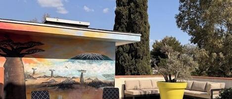 A patio area with a mural, outdoor seating, and a large yellow planter.