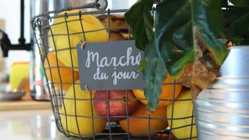 Una encimera de cocina con una cesta de frutas que contiene manzanas y naranjas, una cafetera y una planta en maceta.
