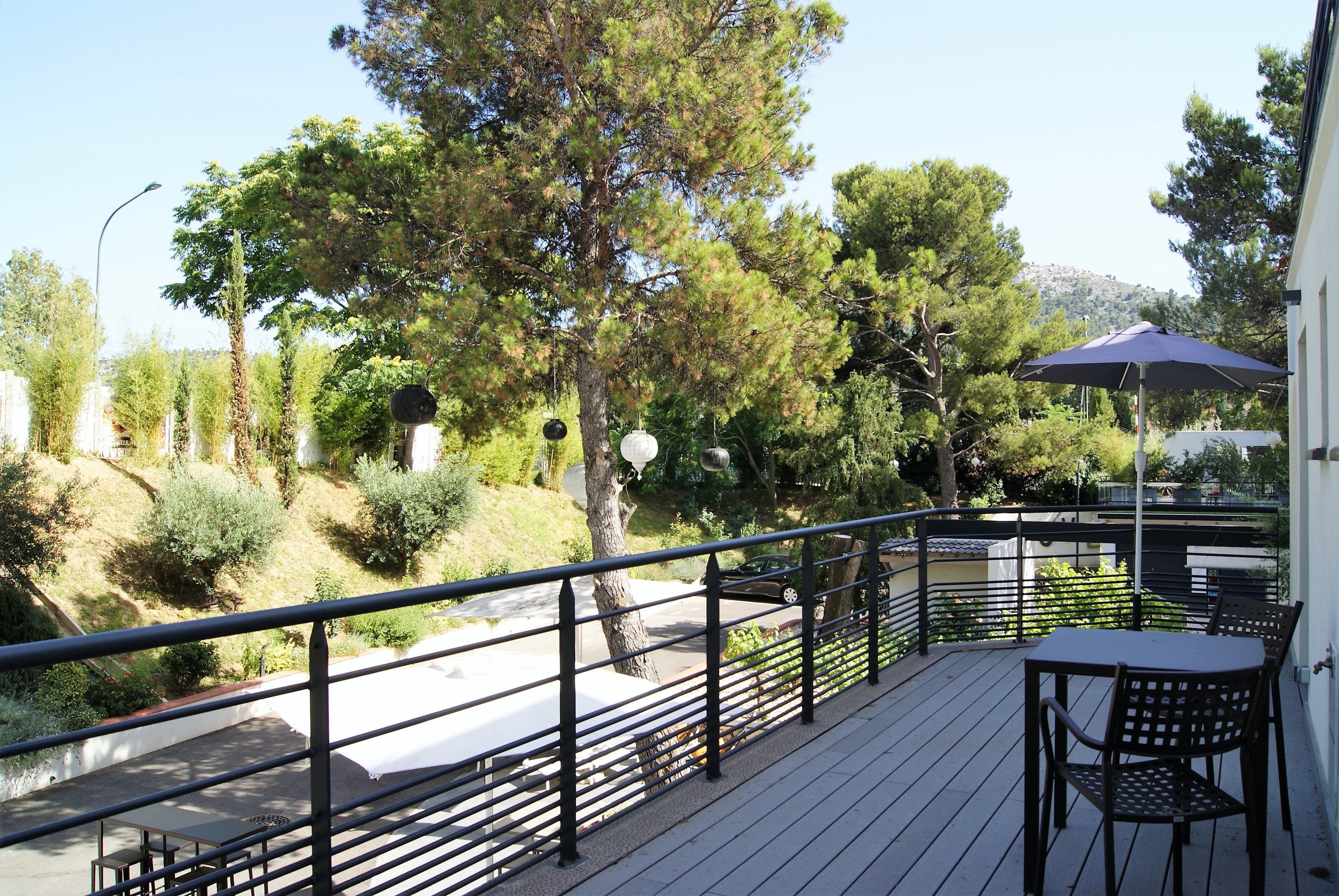 A balcony with a table and chairs, overlooking a road and trees.