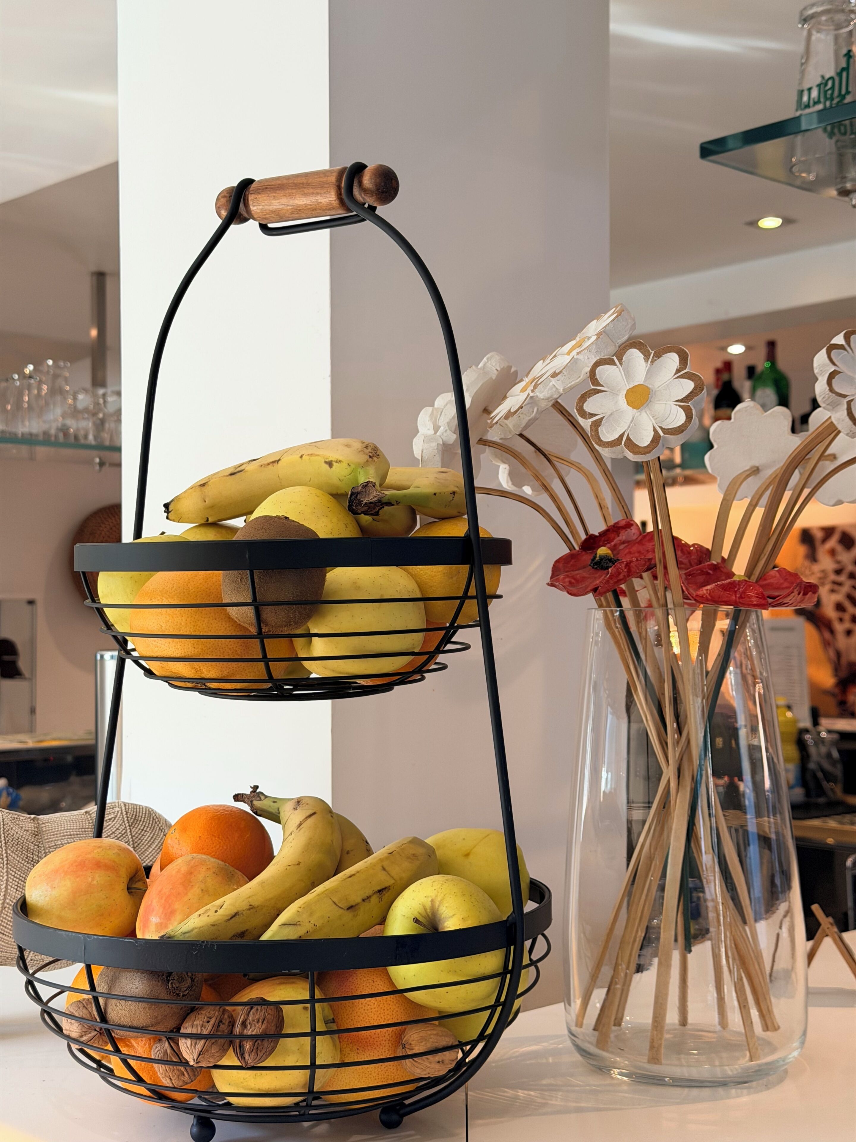 Una frutera de tres niveles con plátanos, manzanas y naranjas.