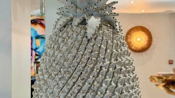A pineapple sculpture with a textured surface and a pointed top, placed on a white surface in a room with a glass partition and a wall-mounted light fixture.