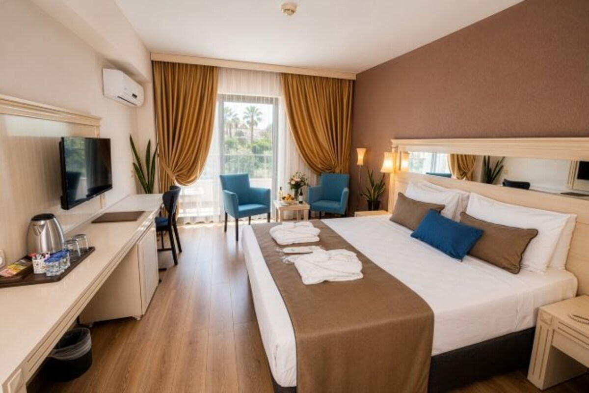 A hotel room with a bed, a desk, a chair, a TV, and a window with curtains.