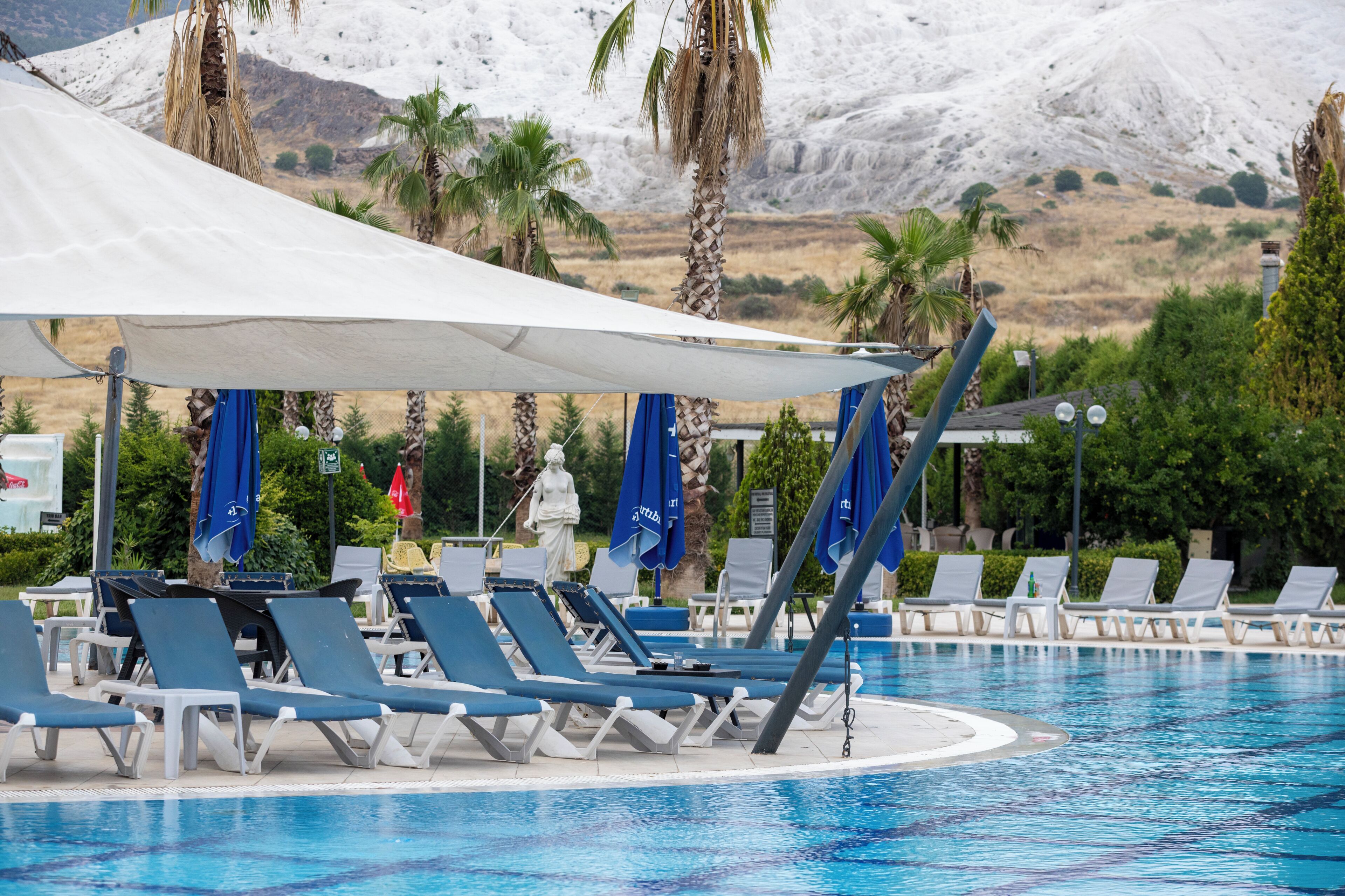 Ein Poolbereich mit Liegestühlen und Sonnenschirmen, einer Statue sowie einer Bergkulisse.