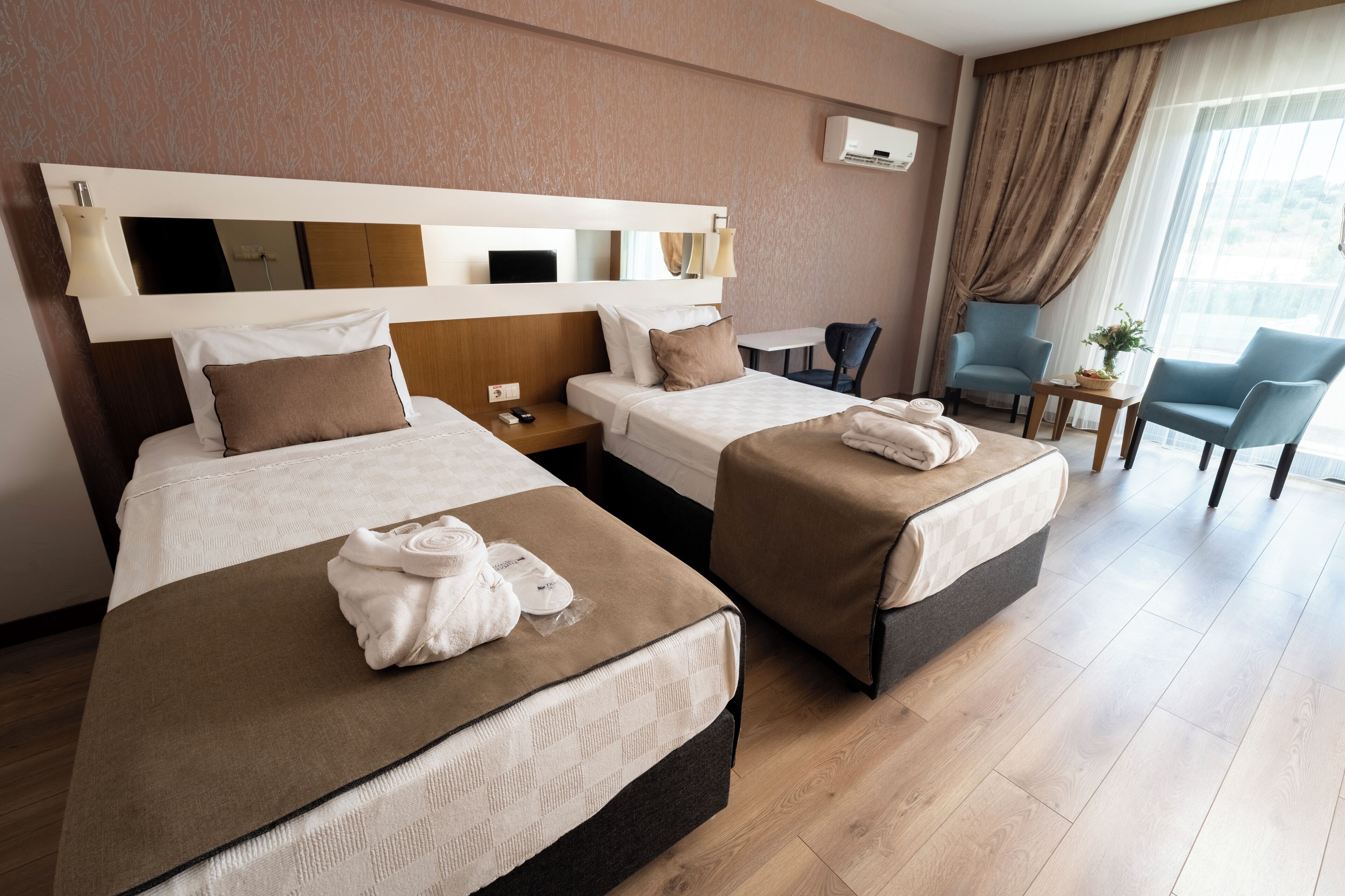 Una camera d'albergo con due letti, una scrivania, una sedia e una finestra con tende.