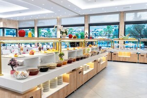 Montaje tipo bufé con varias estaciones de comida, una gran variedad de platos y vistas al exterior a través de amplias ventanas.
