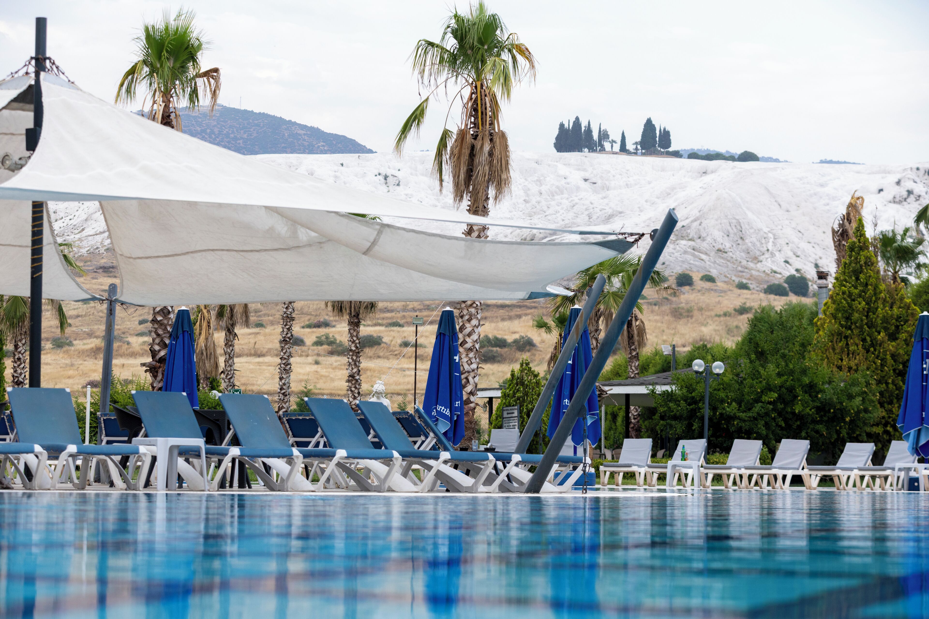 A poolside area with lounge chairs and umbrellas, a white canopy, and a mountainous backdrop.