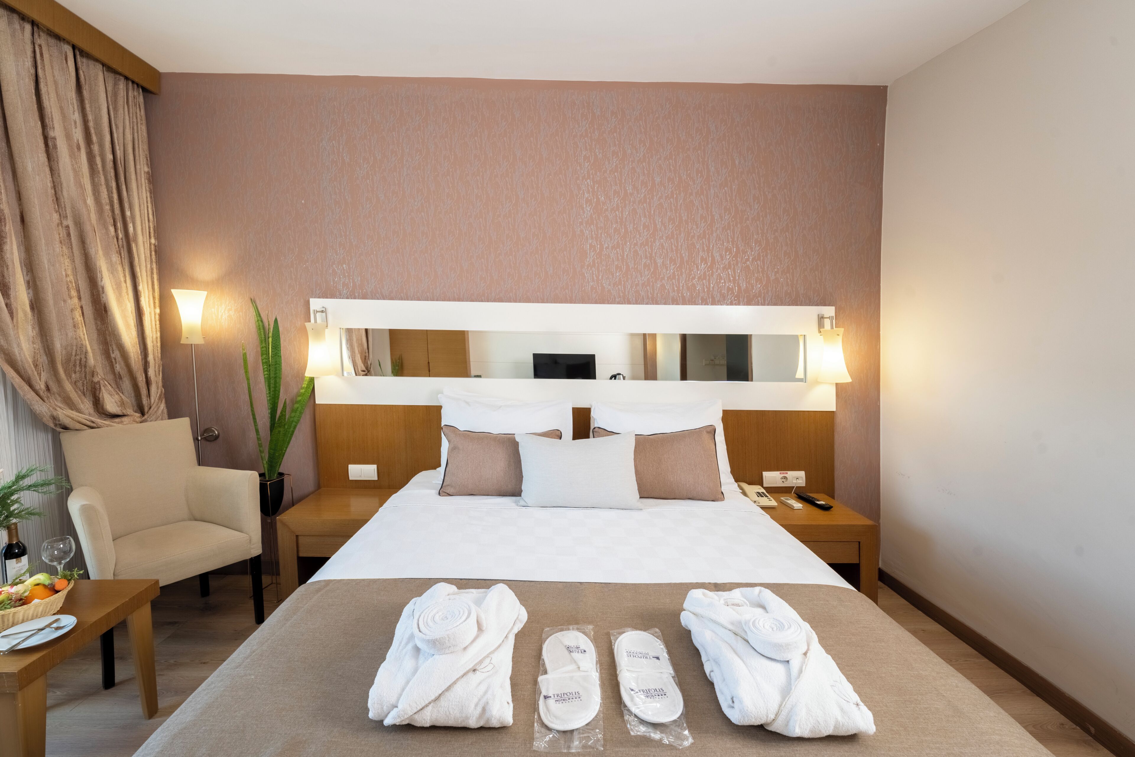 A hotel room with a bed, a chair, a nightstand, and a table with towels and slippers.