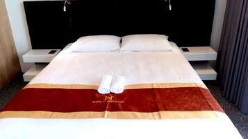Cama bem arrumada com lençóis brancos, duas almofadas e um cobertor vermelho e dourado com o logotipo de um hotel.