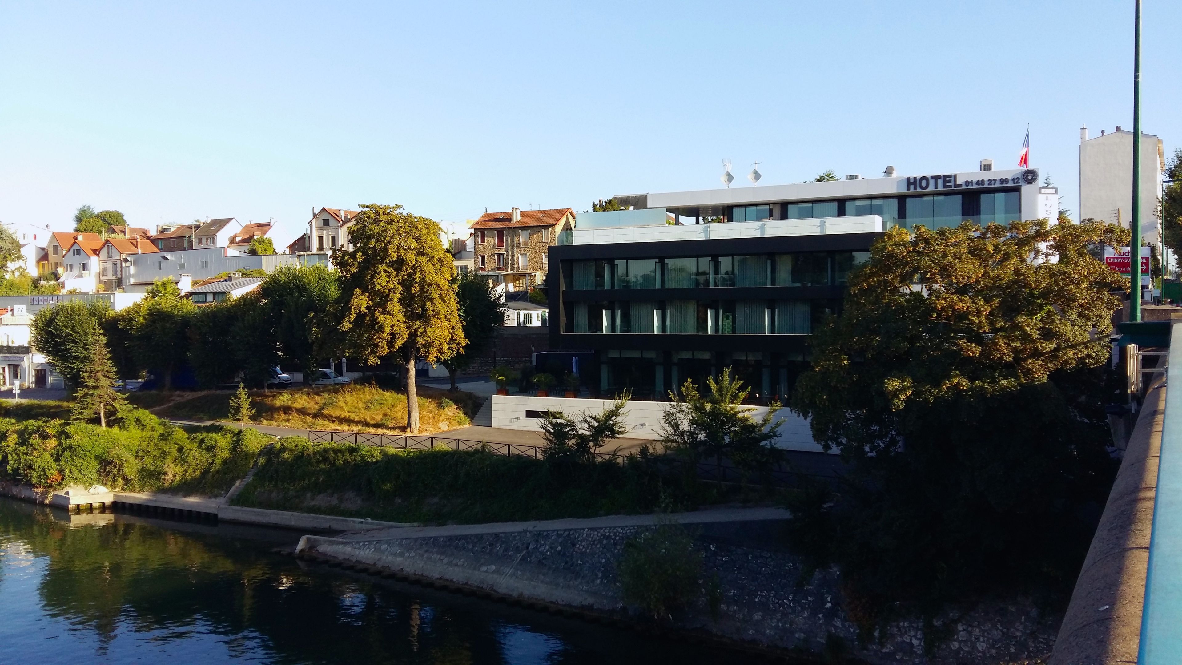 Un hotel moderno con fachada de vidrio, situado cerca de un cuerpo de agua y rodeado de árboles.