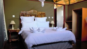 Una cama bien tendida con sábanas blancas y almohadones decorativos, una lámpara de noche y un cabecero de madera rústica.