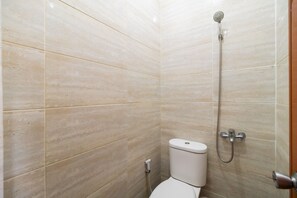 Ein Badezimmer mit beigelfarben gefliesten Wänden, einer weißen Toilette und einer Dusche mit Duschbrause.