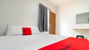 Habitación de hotel con cama, almohada roja, cortina gris, puerta de madera y una pequeña mesa.