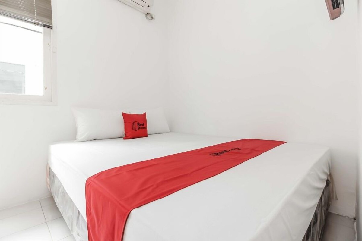 Een hotelkamer met een bed, witte muren, een rood kussen en een rode dekbedovertrek.