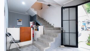 Una escalera que lleva a un balcón, un banco de madera y una recepción con mostrador y un cartel.