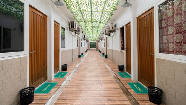 Un pasillo con puertas de madera, felpudos verdes de bienvenida y un techo con plantas colgantes.