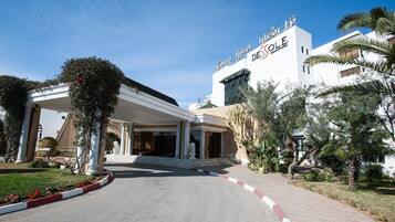 A hotel entrance with a covered walkway, palm trees, and a clear sky.