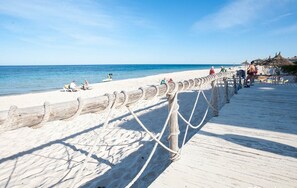 A beach with a wooden boardwalk, beach chairs, and umbrellas.