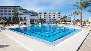 A large swimming pool with clear blue water, surrounded by lounge chairs and umbrellas, with a hotel building in the background. - Hotel Riviera - Family Only (Port El Kantaoui)
