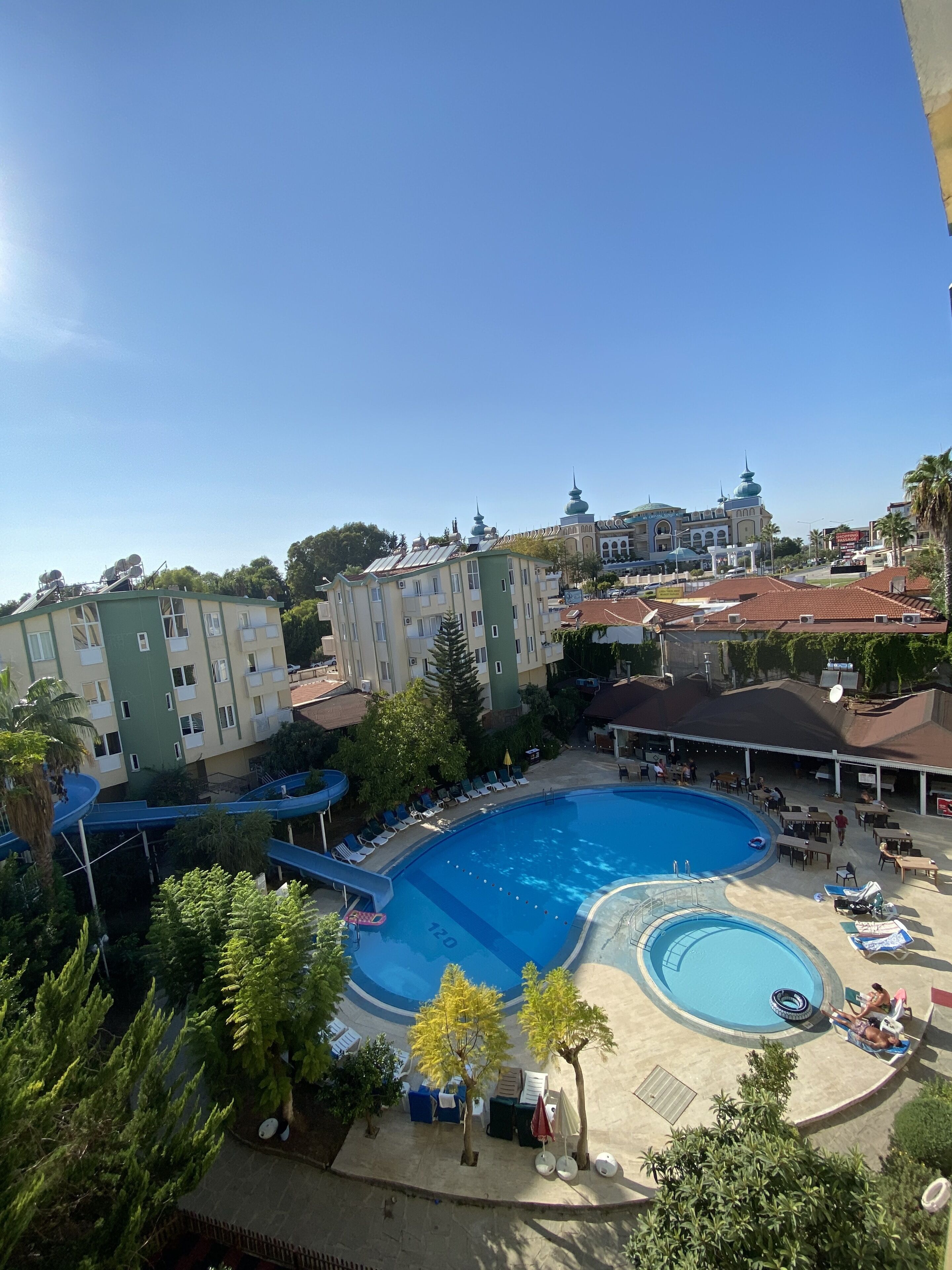 A swimming pool with lounge chairs and umbrellas, surrounded by buildings and trees.