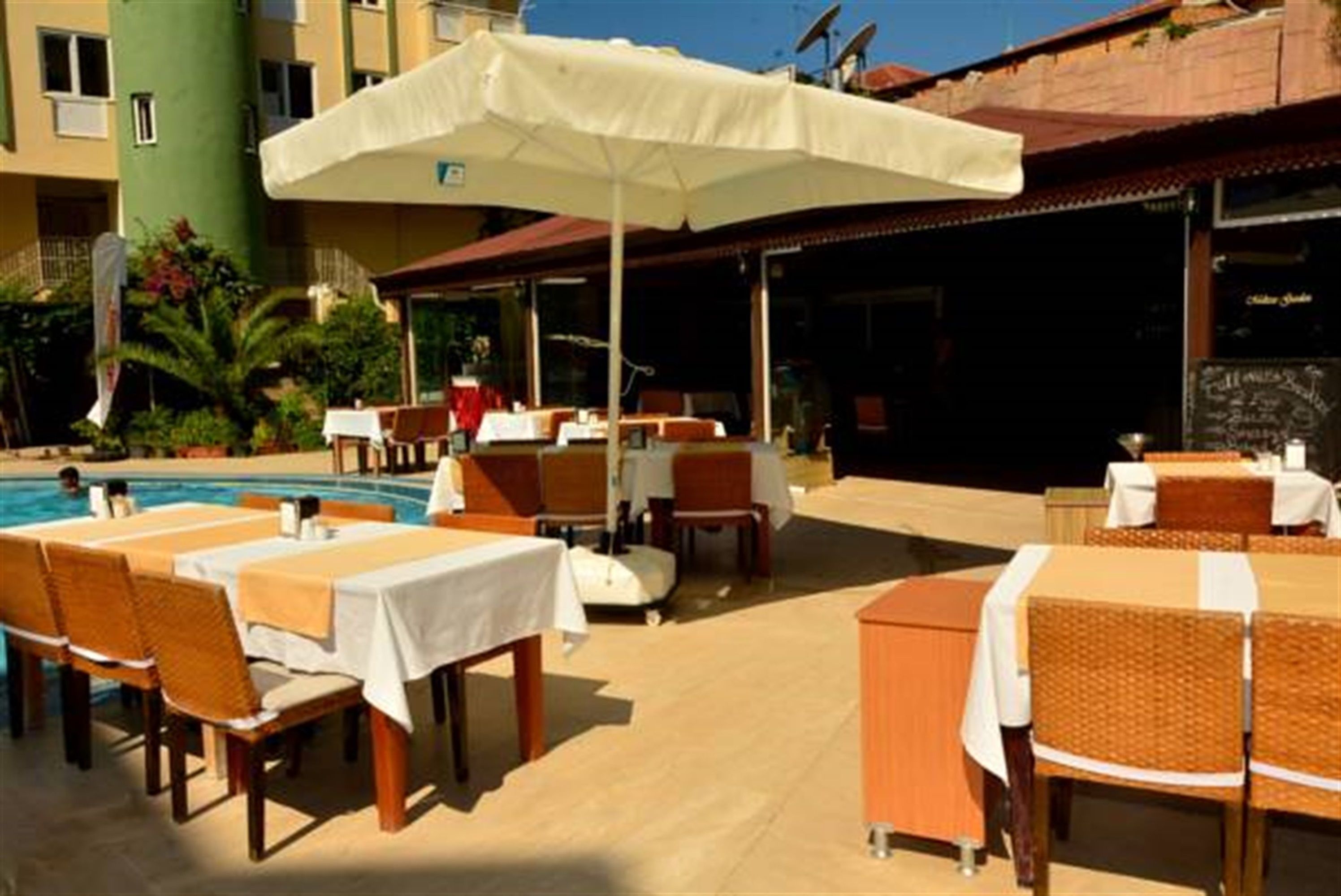 An outdoor dining area with tables and chairs, a pool, and a building in the background.