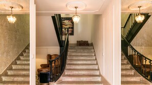 Una imponente escalera con barandal negro, un candelabro y un suelo con diseño.