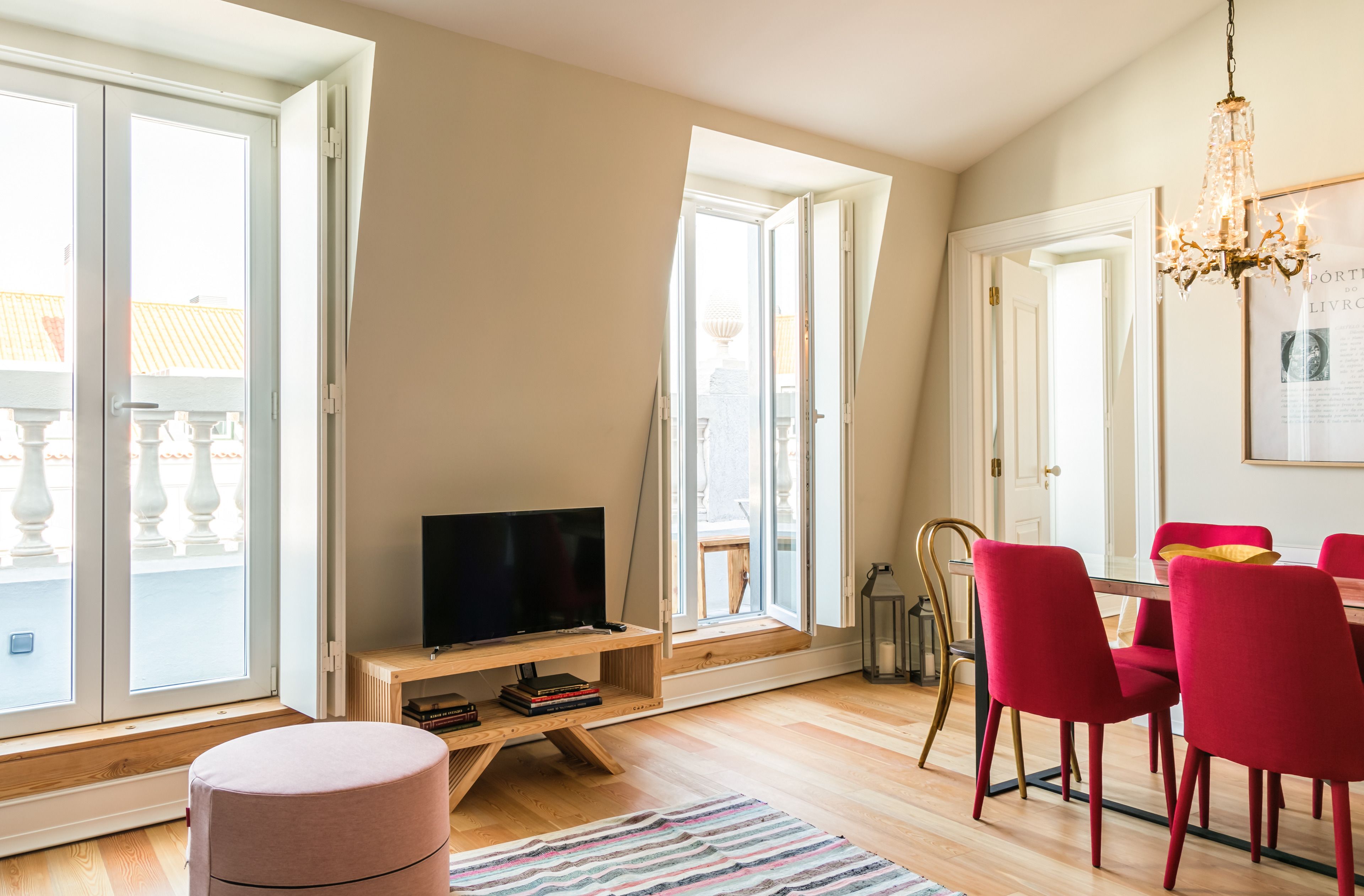 Ein modernes Wohnzimmer mit Fernseher, roten Sesseln, einem Esstisch und großen Fenstern.