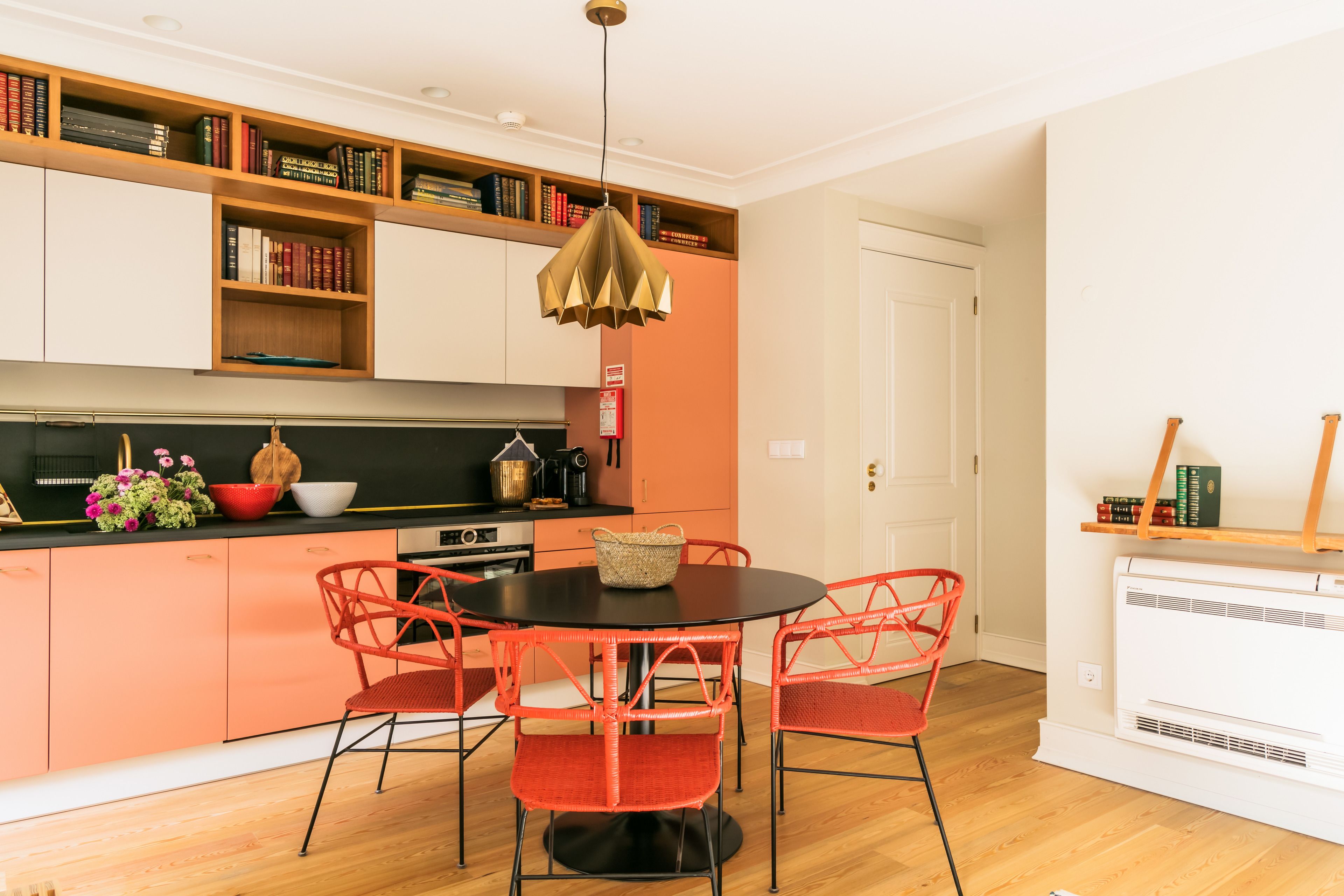 A modern kitchen with a round table and red chairs, a built-in bookshelf, and a white door in the background.