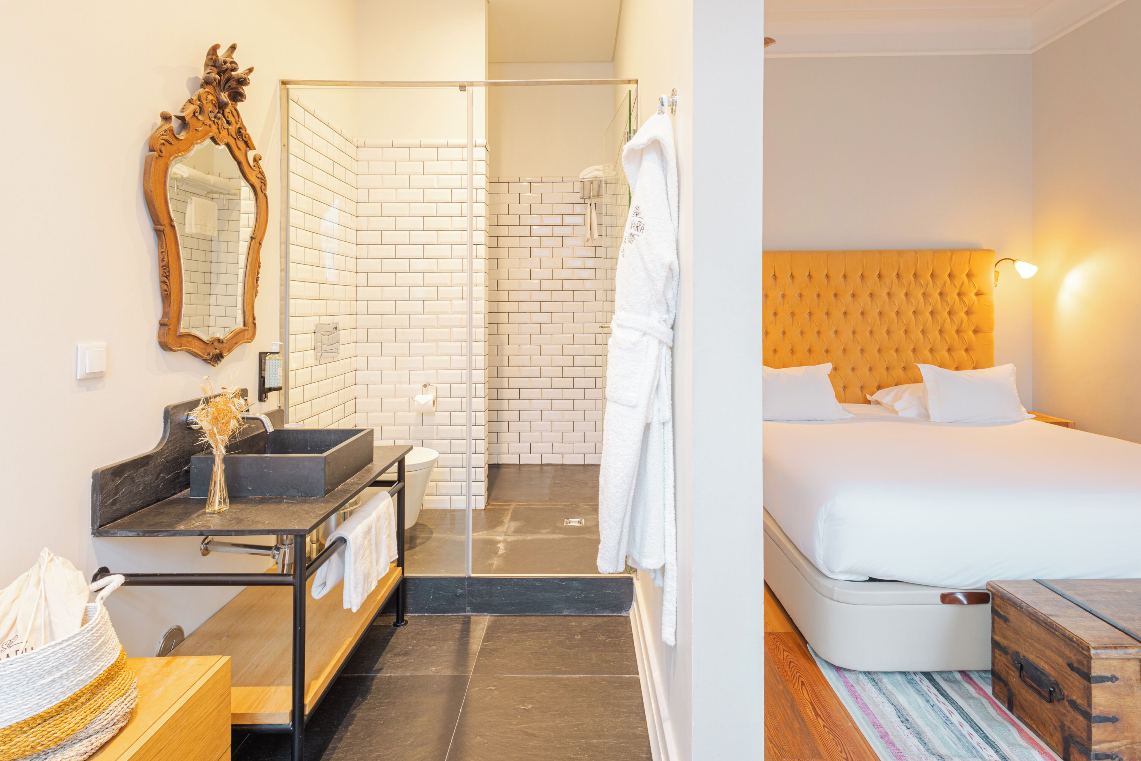 A hotel room with a bathroom, a bed, a wooden headboard, and a mirror.