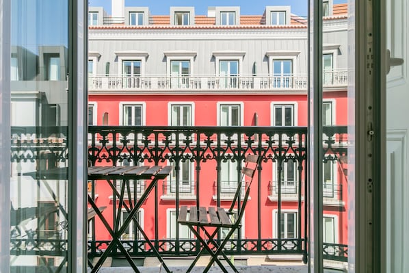A balcony with a table and chair, overlooking a row of red buildings with balconies. - Almaria Ex Libris Chiado (Lisbon)