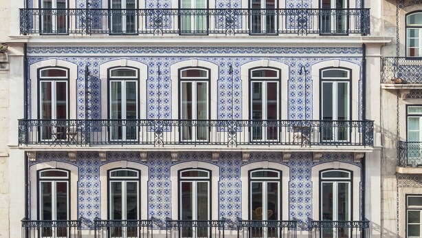Un edificio de varios pisos con baldosas azules y blancas estampadas, varios balcones y toldos sobre las ventanas de la planta baja.