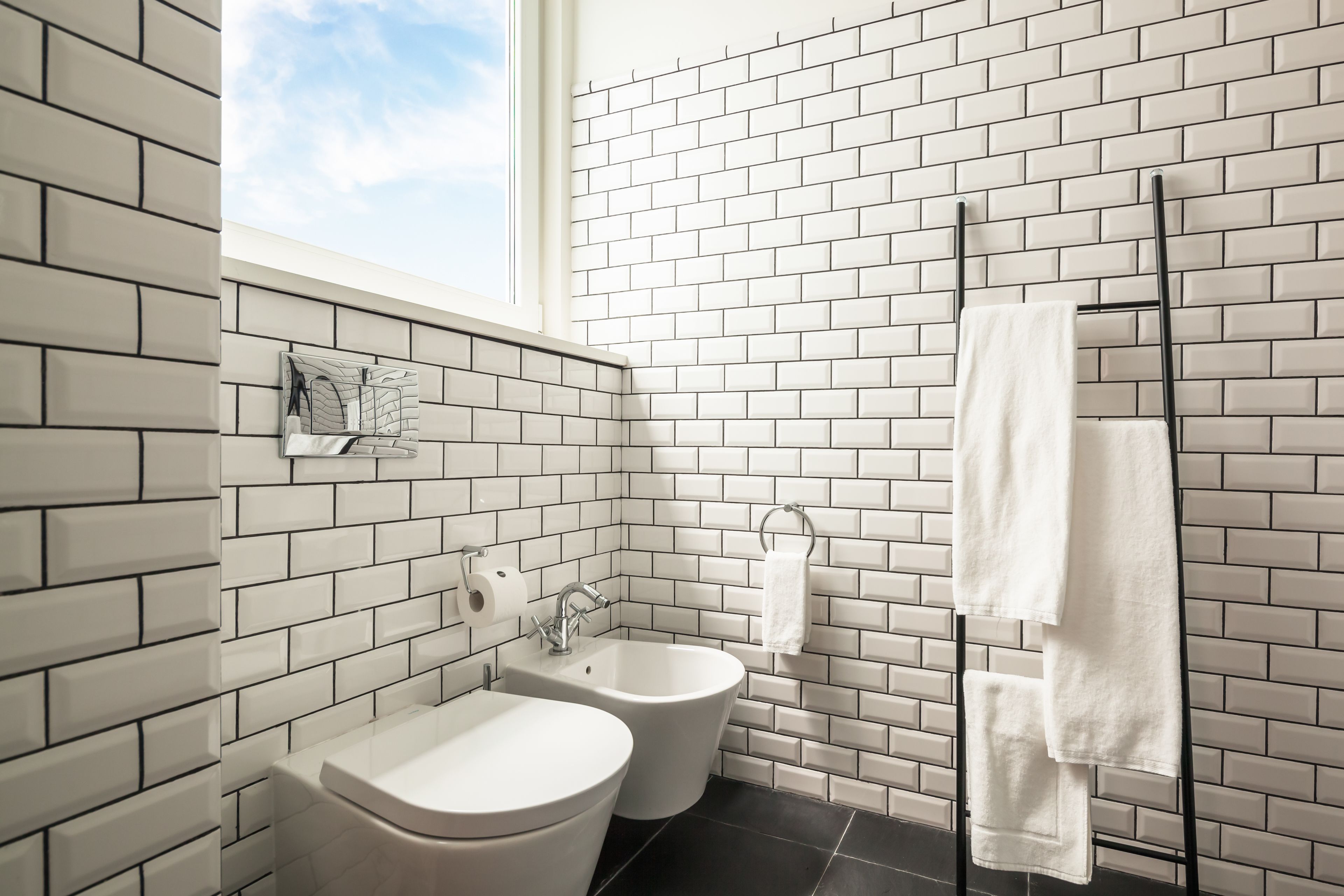 Un baño moderno con azulejos blancos tipo metro, un bidé, un inodoro y un perchero para toallas.