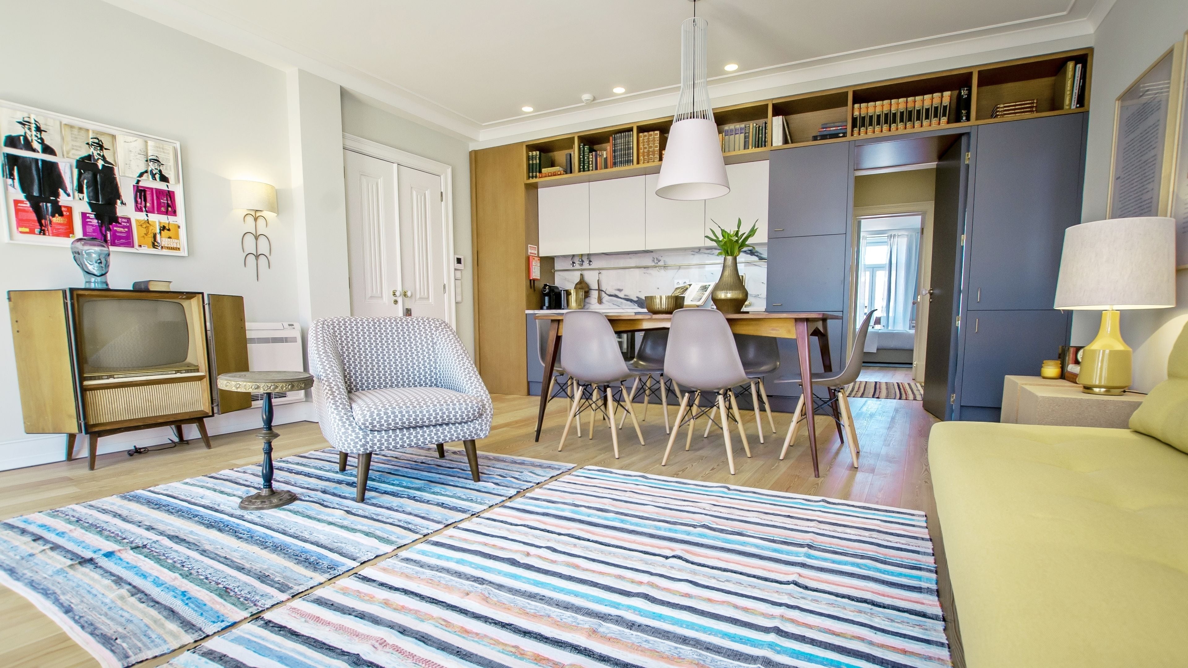 Uma sala de estar moderna com um sofá, uma poltrona estampada, um tapete listrado, uma televisão e uma área de jantar com cadeiras e uma mesa.