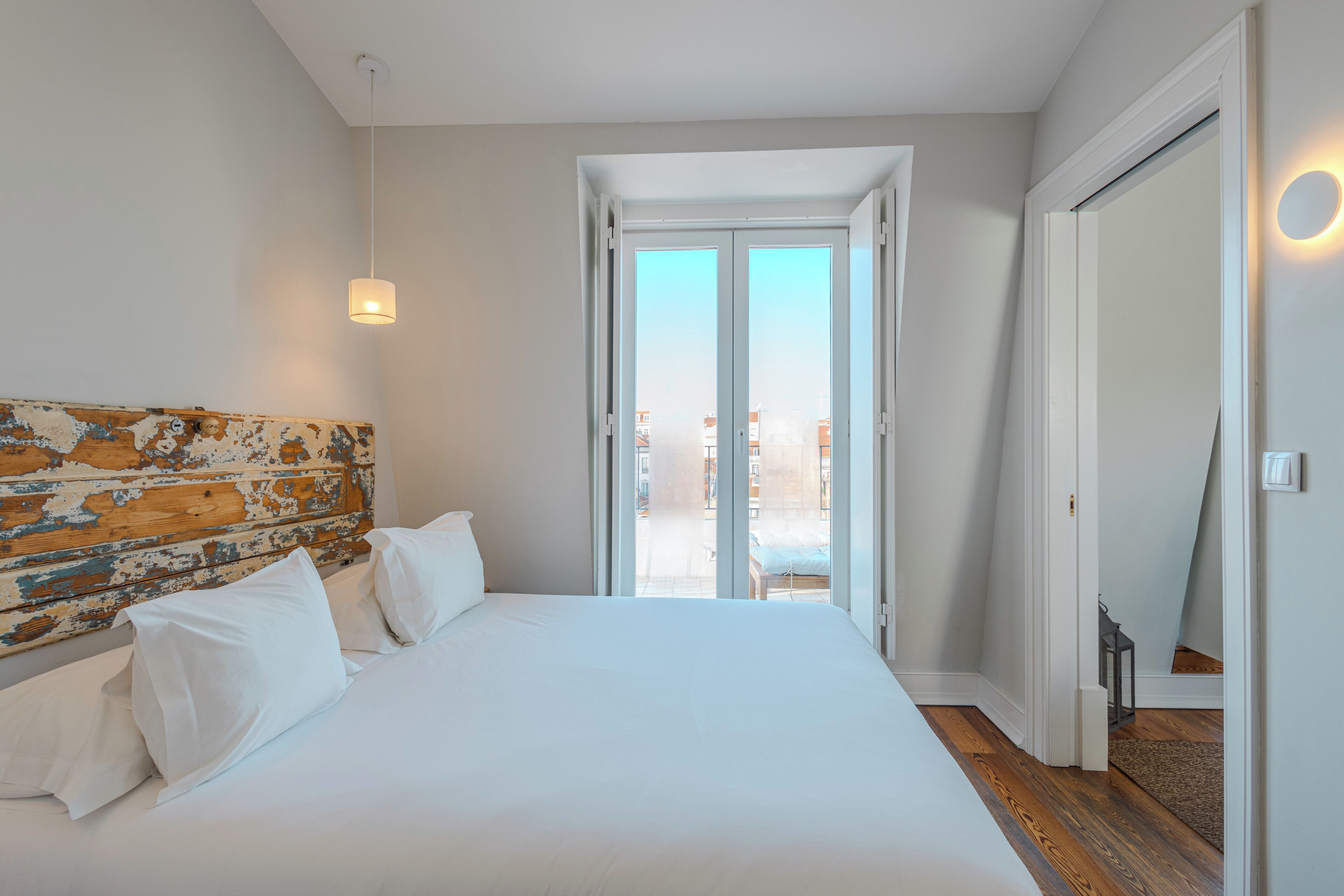 Un dormitorio con una cama grande, cabecera de madera, puerta corrediza de vidrio al balcón y una mesita cerca de la puerta.