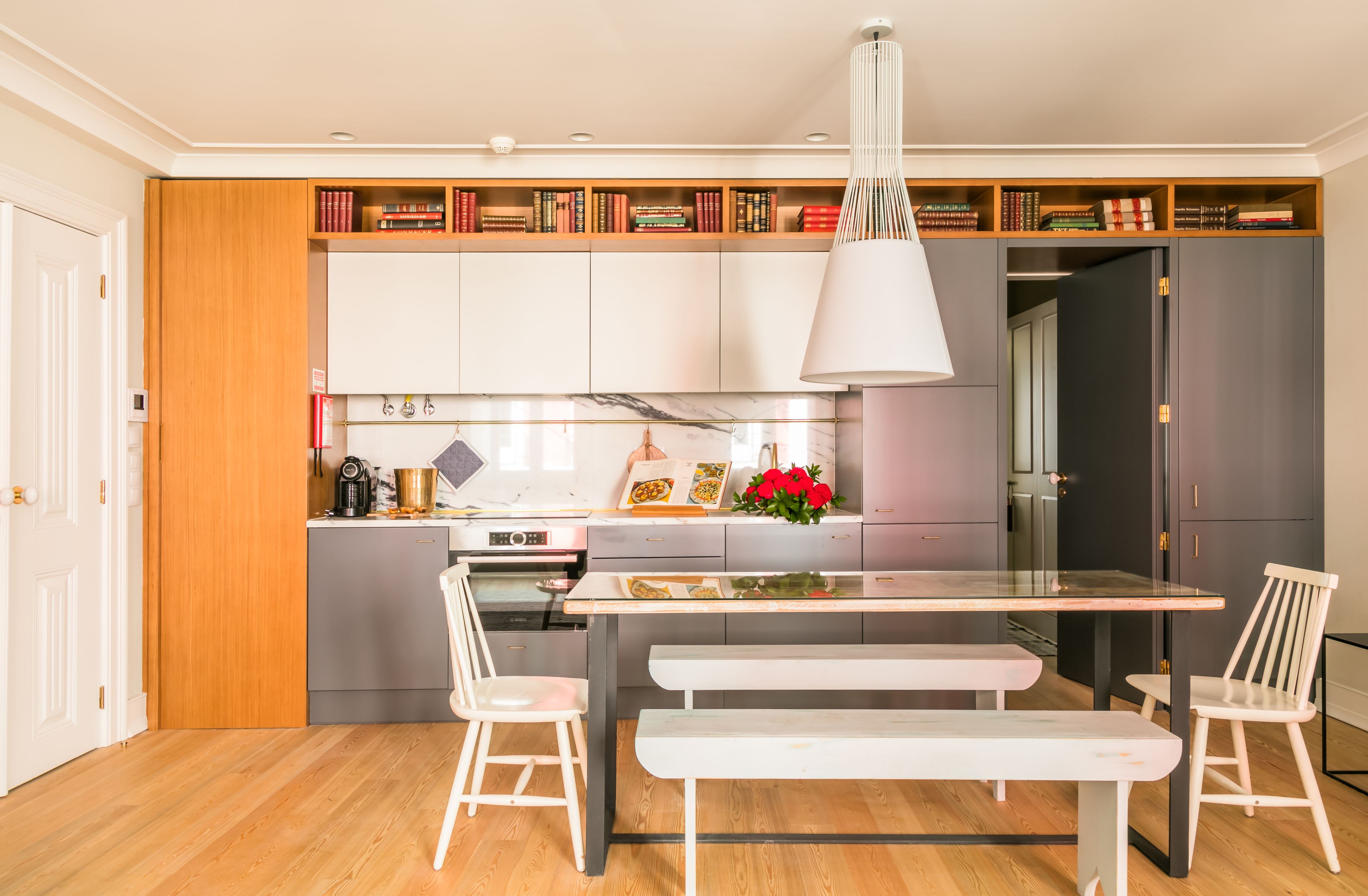 Une cuisine moderne avec des meubles blancs, un plan de travail en marbre et un coin repas comprenant une banquette et des chaises.