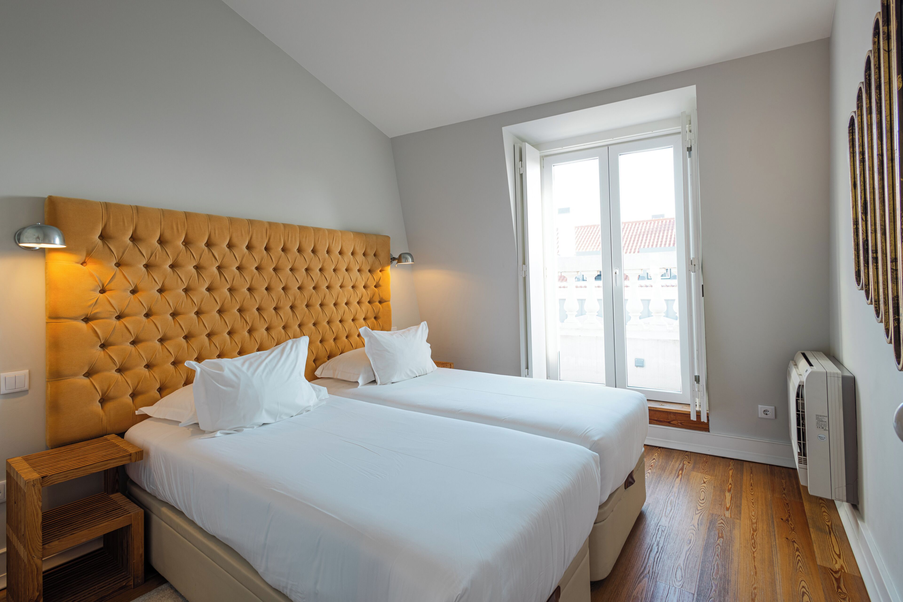 A bedroom with two beds, a wooden headboard, bedside lamps, a window, and a radiator.