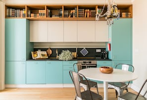 Una cocina con armarios verde azulado, una mesa de comedor blanca y una araña.