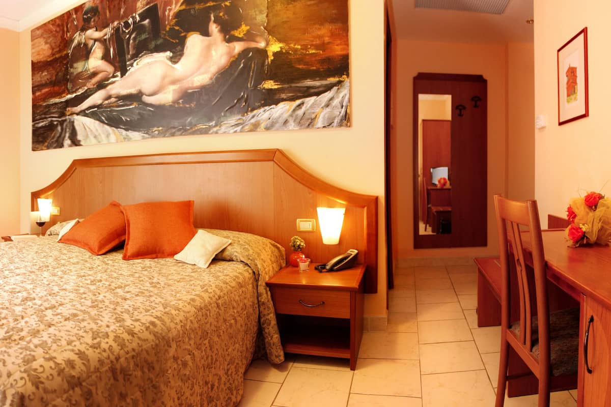 Ein Hotelzimmer mit einem großen Bett, einem Nachttisch mit Lampe, einer Holzkommode und einem Gemälde an der Wand.
