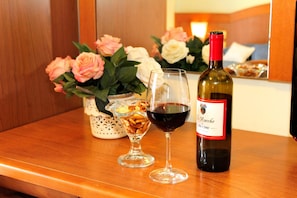 Una botella de vino Rocche Piccini, una copa de vino tinto y un vaso decorativo con frutos secos sobre una mesa de madera.