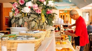 A buffet setup with a floral centerpiece, plates, and baskets of food. - Hotel Ariston (Grosseto)