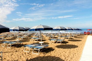 Una playa con filas de tumbonas y sombrillas, un paseo marítimo de madera y el océano al fondo.