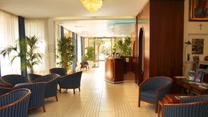 A hotel lobby with a reception desk, several seating areas with chairs, and potted plants. - Hotel Ariston (Grosseto)