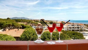 Two martini glasses with red drinks and a dessert glass with a dessert on a balcony overlooking a coastal town. - Hotel Ariston (Grosseto)