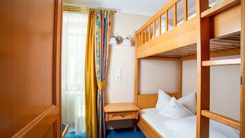 A compact hotel room with a bunk bed, a small bedside table, and a window with curtains.