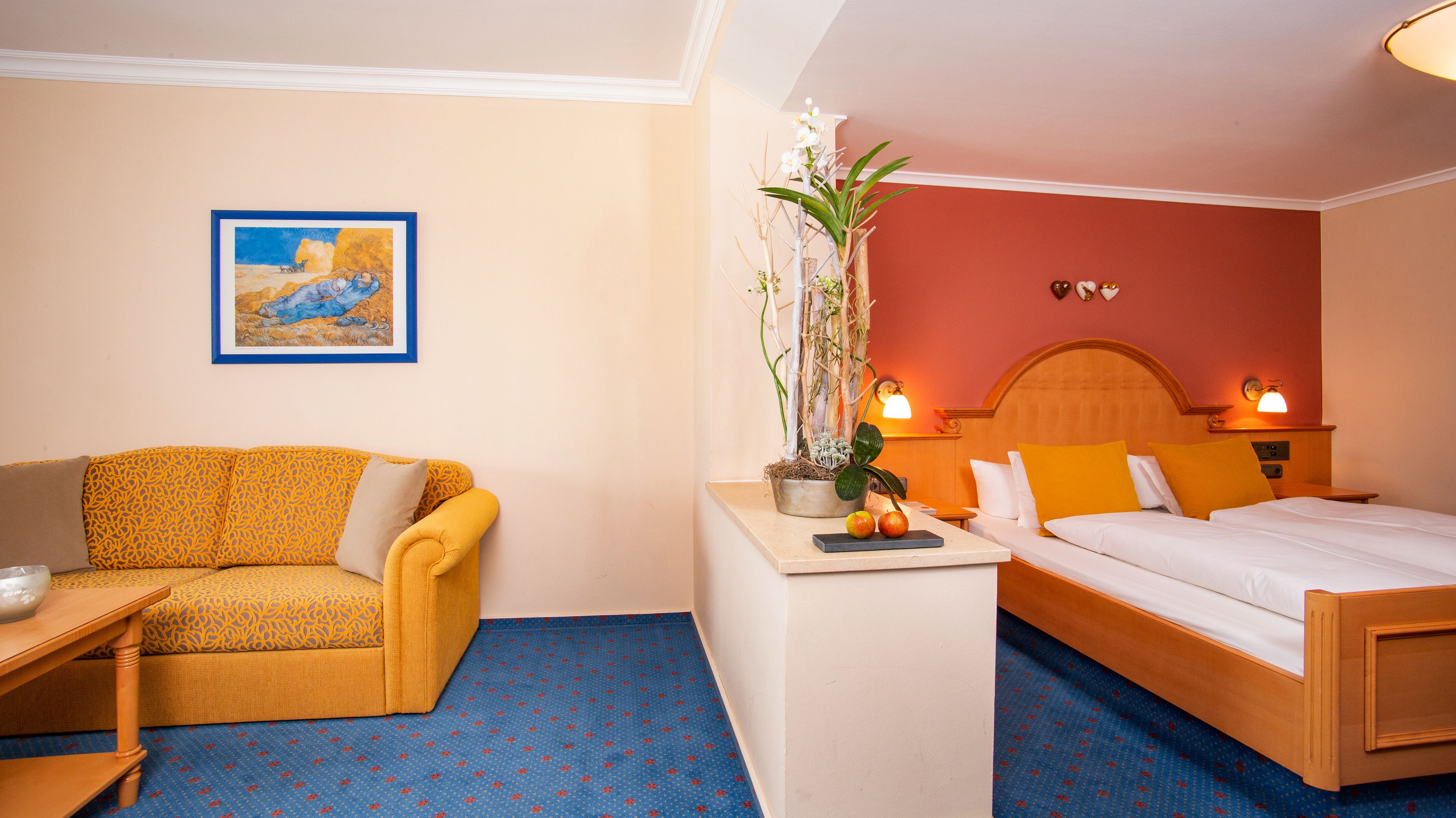 Quarto de hotel com cama, sofá, uma mesinha e um vaso de planta.