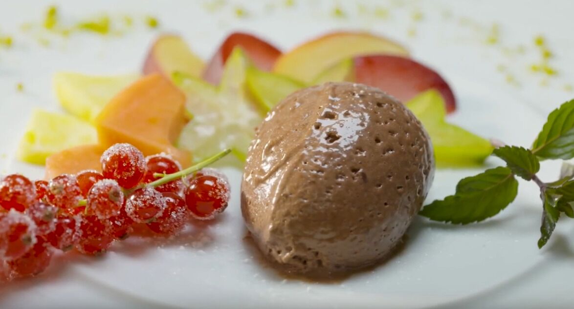 A dessert plate with a scoop of chocolate ice cream, accompanied by fresh fruit slices and red currants.