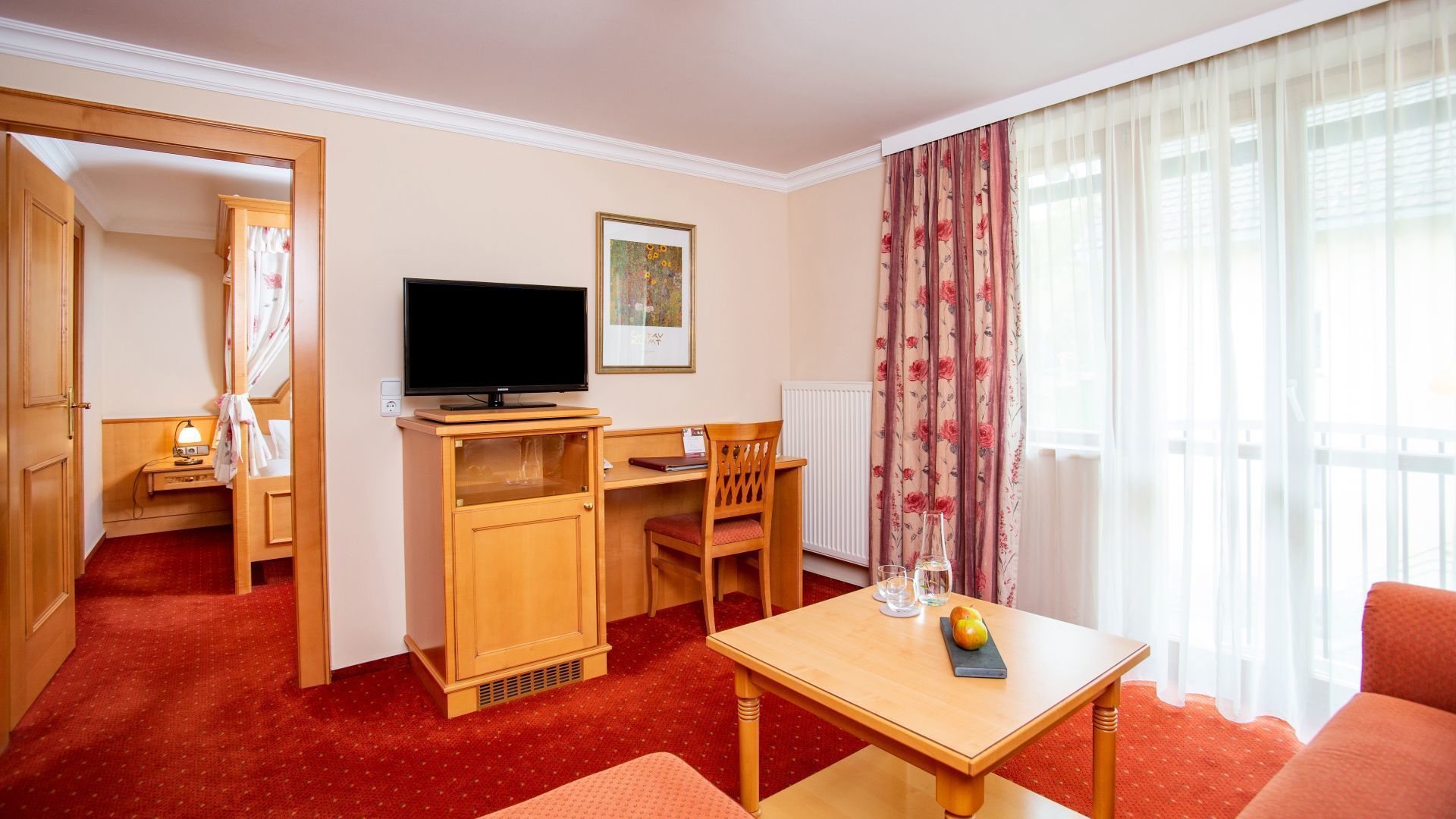 Habitación de hotel con un escritorio de madera, televisor, una silla, un sofá y una mesa de comedor con fruteros.