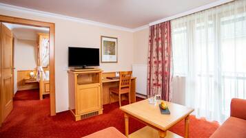 Habitación de hotel con un escritorio de madera, televisor, una silla, un sofá y una mesa de comedor con fruteros.