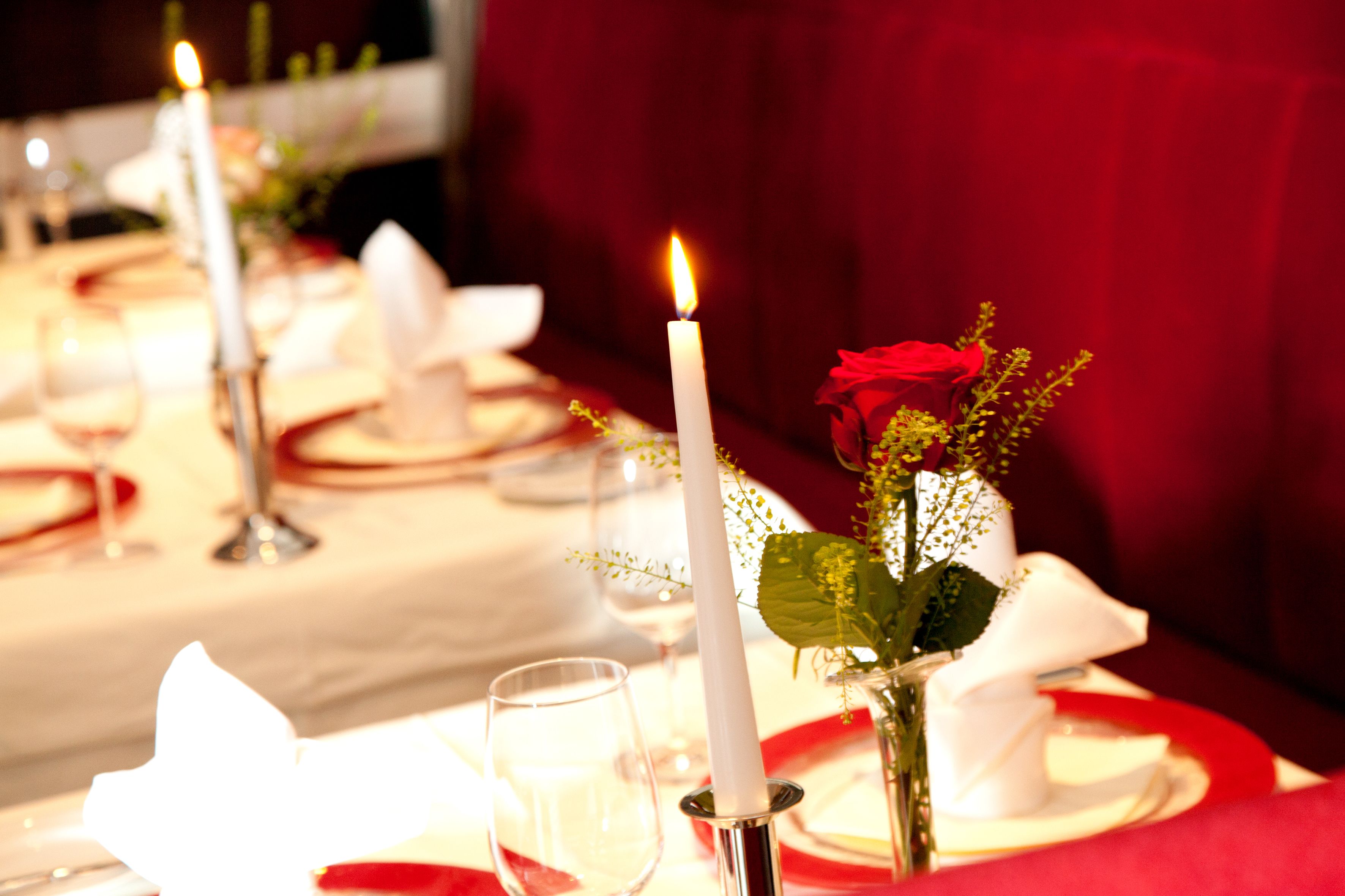 A dining table set with white napkins, red tablecloths, and a lit candle.