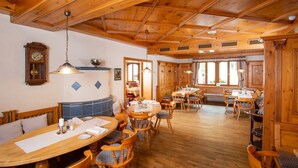 A wooden interior with multiple dining tables and benches, a clock on the wall, and a large window with curtains. - Hotel St Florian (Frauenau)